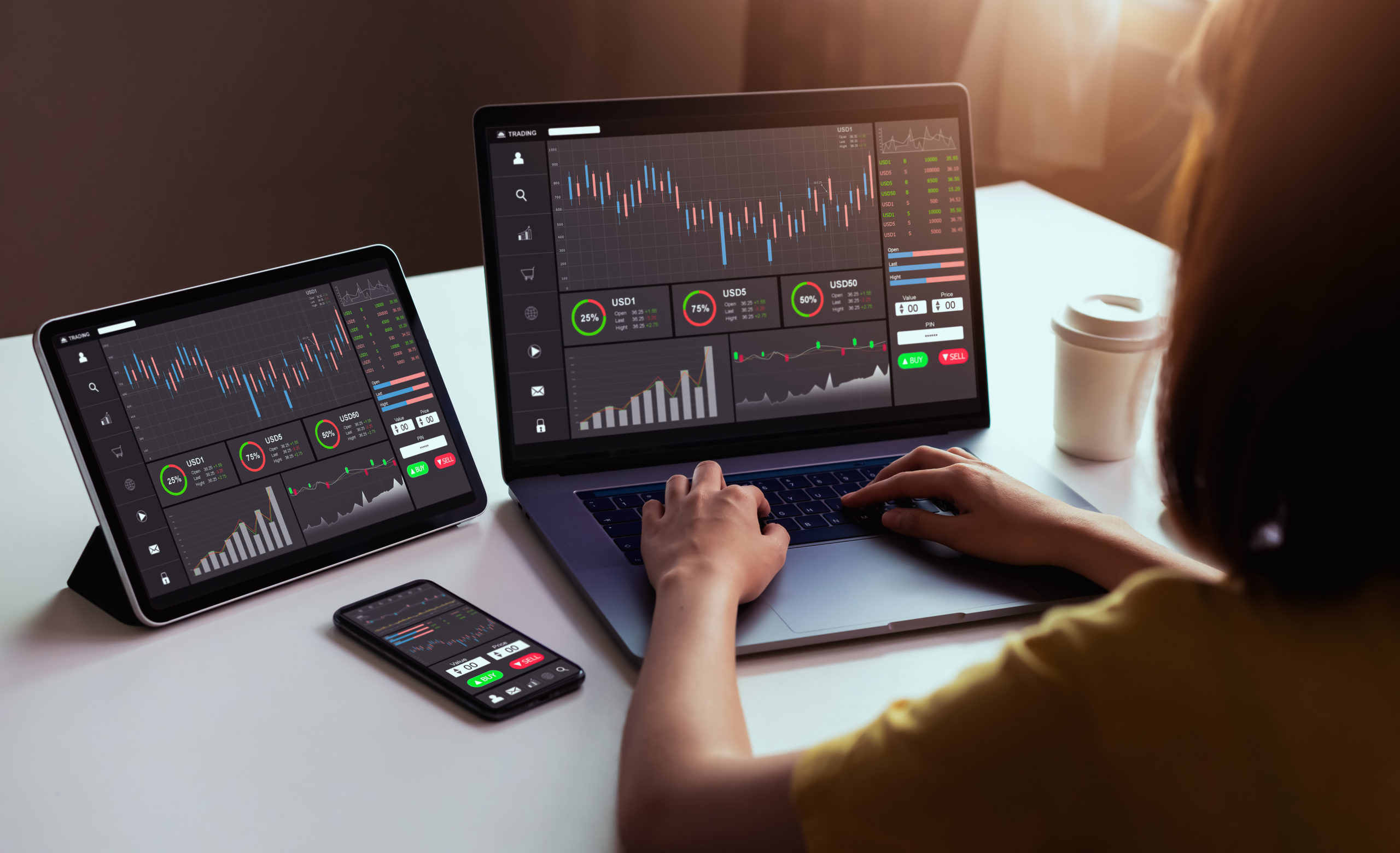 Business person working at desk on laptop with i-pad, reviewing graphs and charts on screen